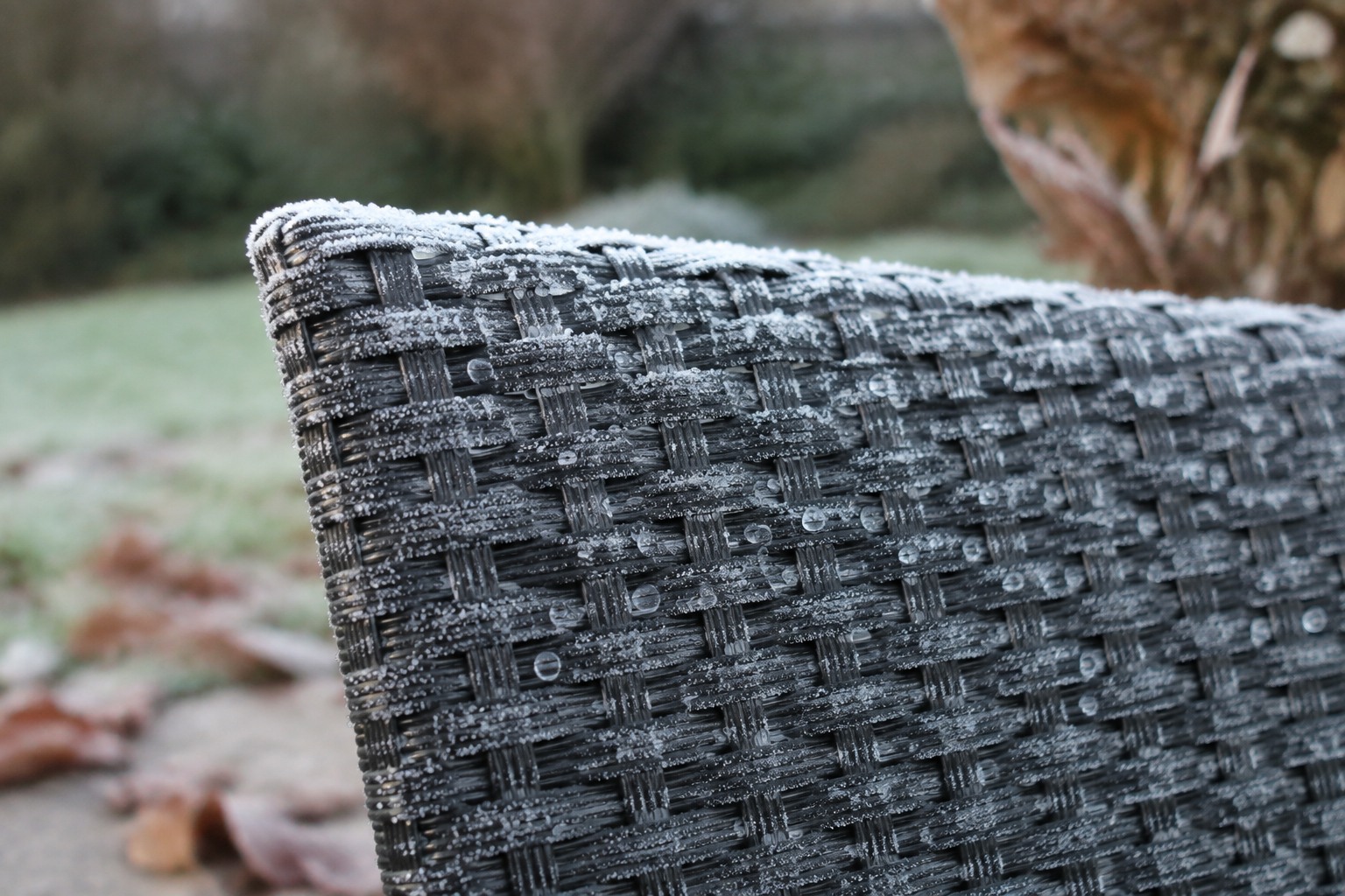 Gros plan sur une chaise de jardin en résine tressée couverte de givre et de gouttes gelées