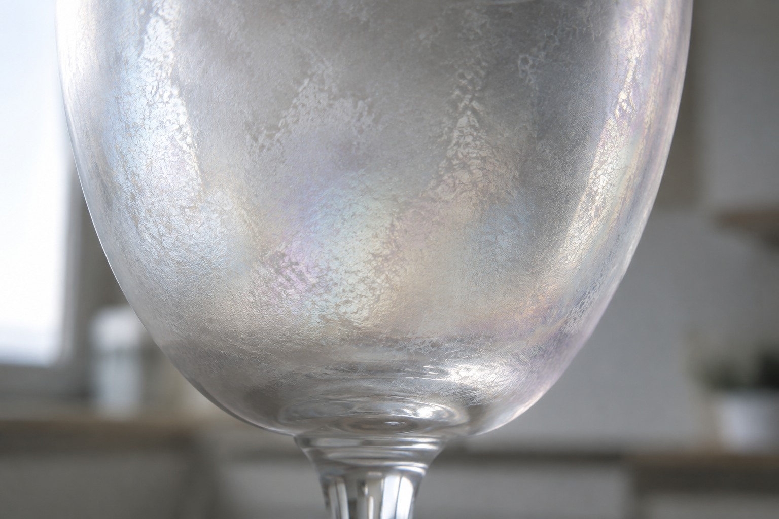 Gros plan sur un verre corrodé au voile laiteux et légèrement irisé, vu en lumière rasante
