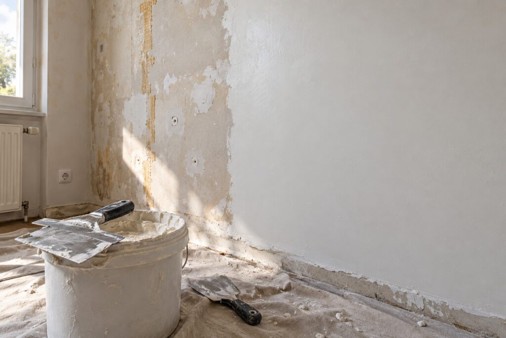 Mur en partie recouvert d'enduit de lissage frais, couteau à enduire large posé sur un seau