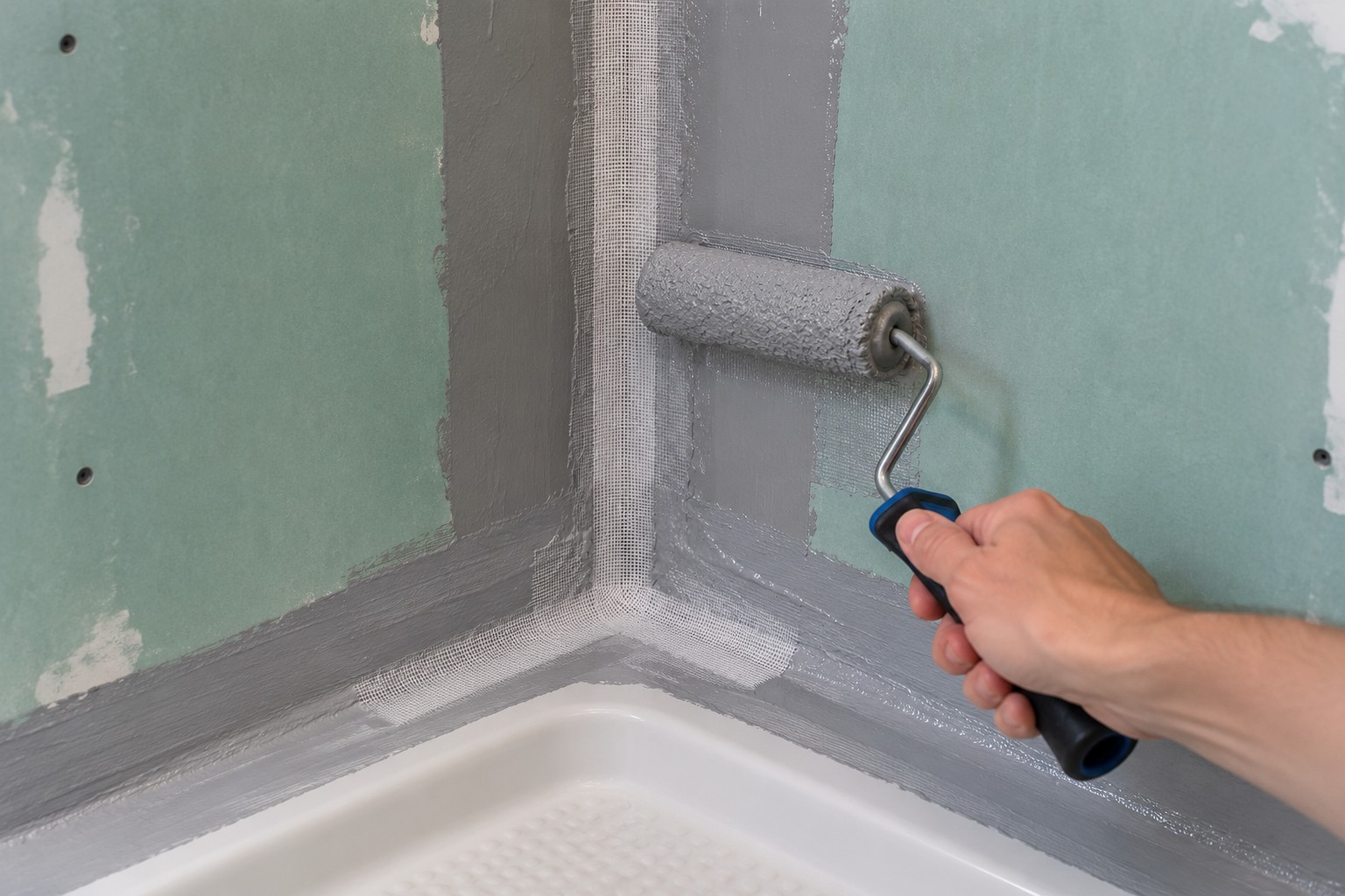 Protection à l'eau sous carrelage appliquée au rouleau dans l'angle d'une douche avec une bande de renfort sur des plaques hydrofuges